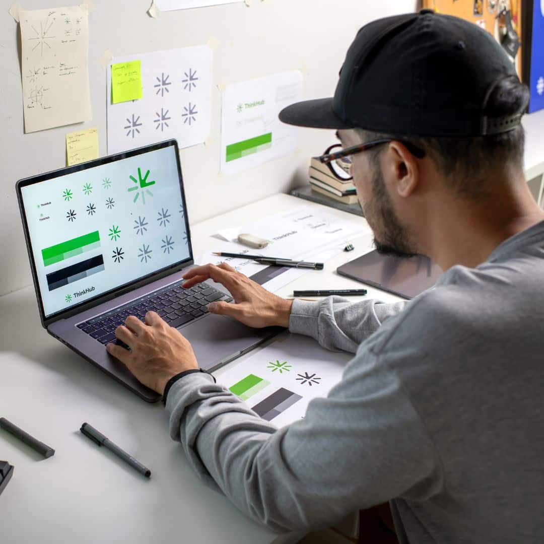 Designer working on logo design and brand guidelines on a laptop at a creative workspace